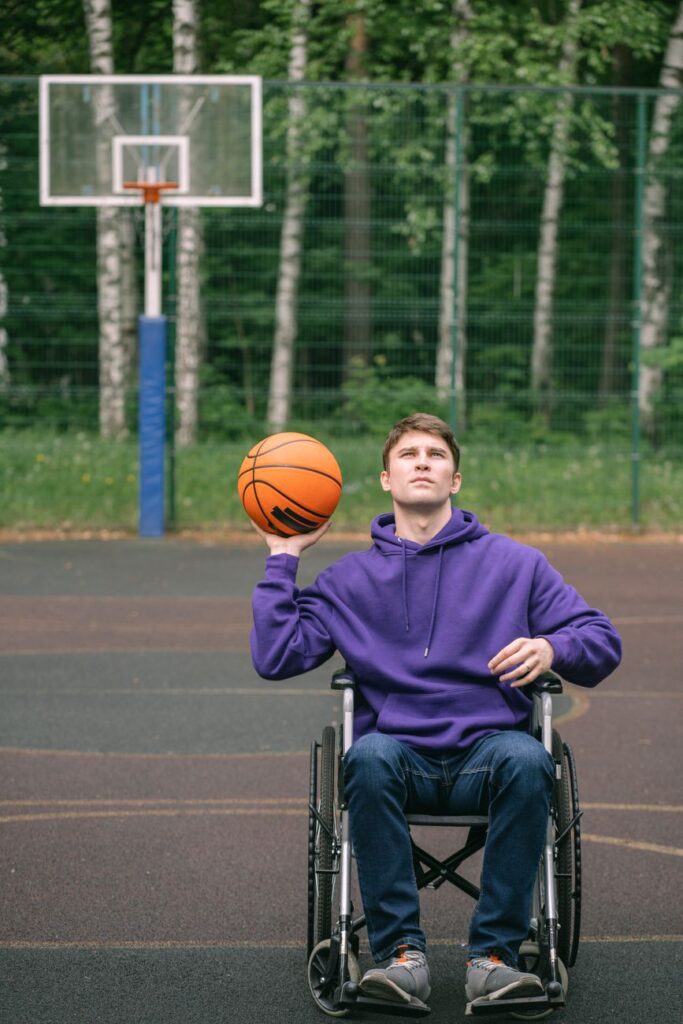 Young man in wheelchair playing basketball on an outdoor court, displaying determination and skill.