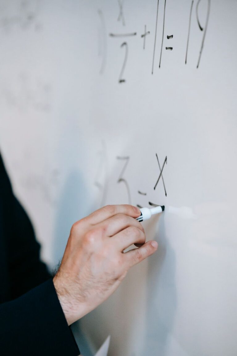 An educator uses a marker to solve equations on a whiteboard, demonstrating math skills.