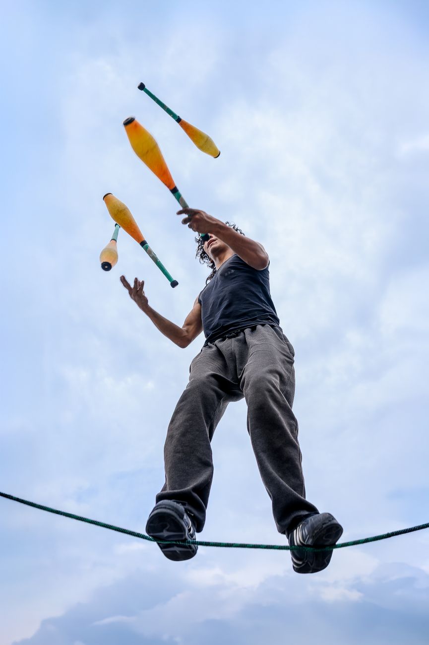 A skilled performer juggles on a tightrope, captured against a dramatic cloudy sky, showcasing balance and dexterity.