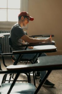Young man concentrating on writing during a lecture in a sunlit classroom.
