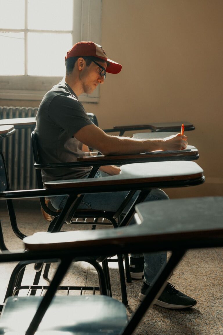 Young man concentrating on writing during a lecture in a sunlit classroom.